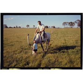 Man on horse with boy standing on ground